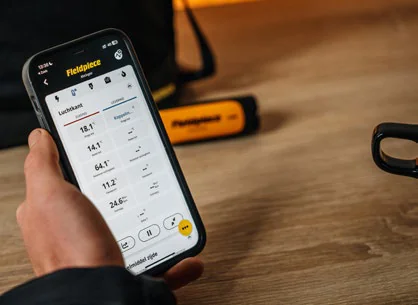 Telefon z aplikacją Job Link®, na ekranie kolumna odczytów; obok na blacie sonda Fieldpiece